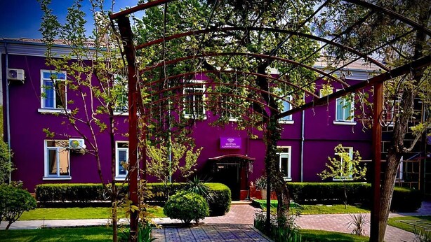 A purple building with a reception area, a paved pathway, and well-maintained greenery. - Armon Apart Hotel (Khujand)