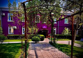 Un edificio morado con recepción, un camino empedrado y jardines bien cuidados.