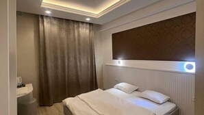 A modern bedroom with a bed, a bedside table, a nightstand, and a large window with curtains. - Armon Apart Hotel (Khujand)