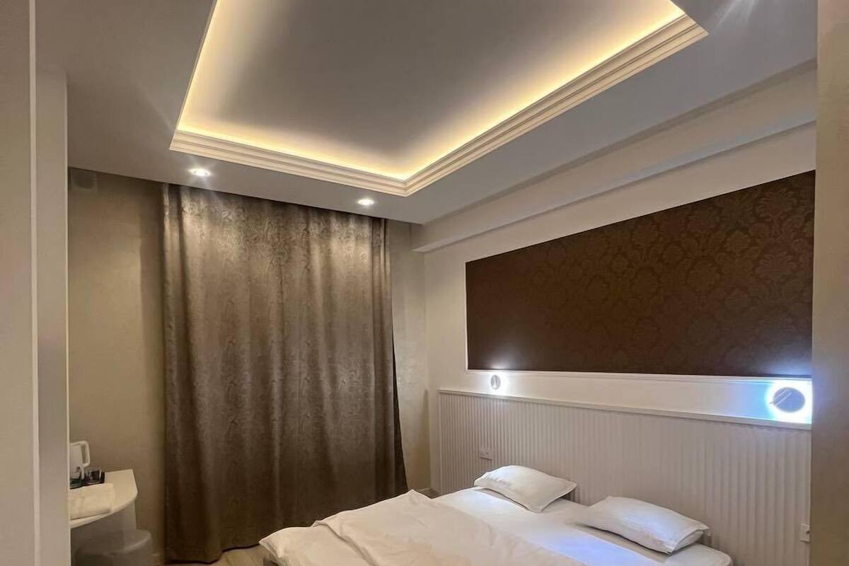 A modern bedroom with a bed, a bedside table, a nightstand, and a large window with curtains.