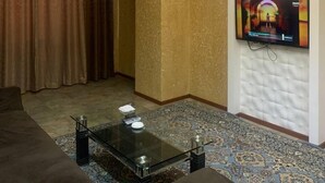 A living room with a chandelier, a television mounted on the wall, a patterned carpet, and a sofa. - Armon Apart Hotel (Khujand)