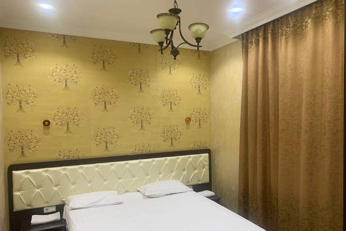 A hotel room with a bed, a nightstand, a wall-mounted lamp, and a curtain.
