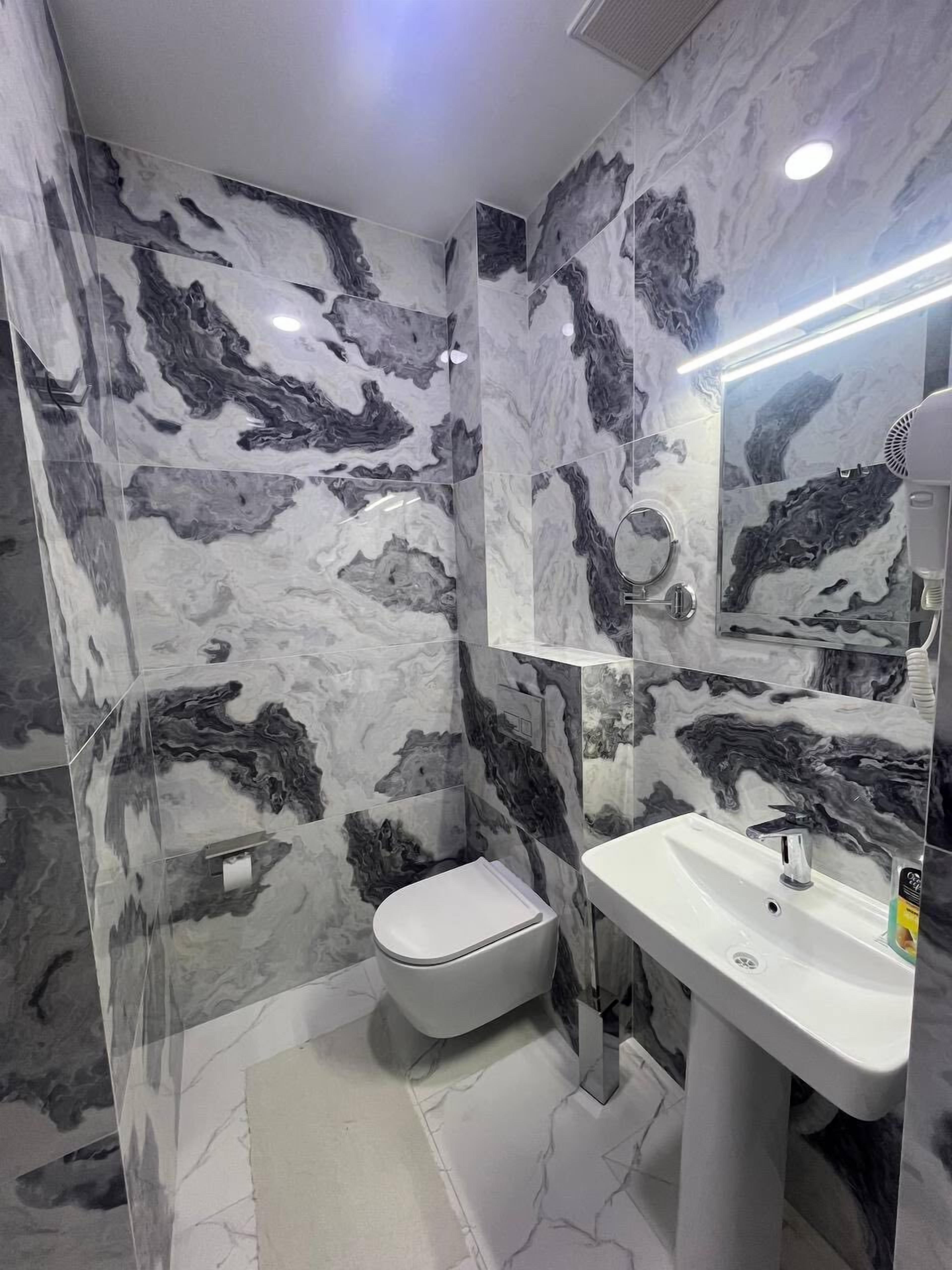 Un baño con paredes de mármol, un inodoro, un lavabo y un espejo.