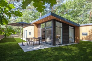 A modern house with a patio, a dining area, and a large window. - Lodge in Bospark with Sauna & Garden (Mierlo)