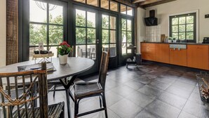 A spacious kitchen with large windows, wooden beams, and a round dining table with wicker chairs. - Lush holiday home with a private Hot Tub (Zeeland)