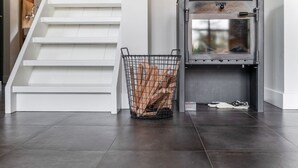 A modern interior with a staircase, a metal basket with logs, and a wood-burning stove. - Lush holiday home with a private Hot Tub (Zeeland)