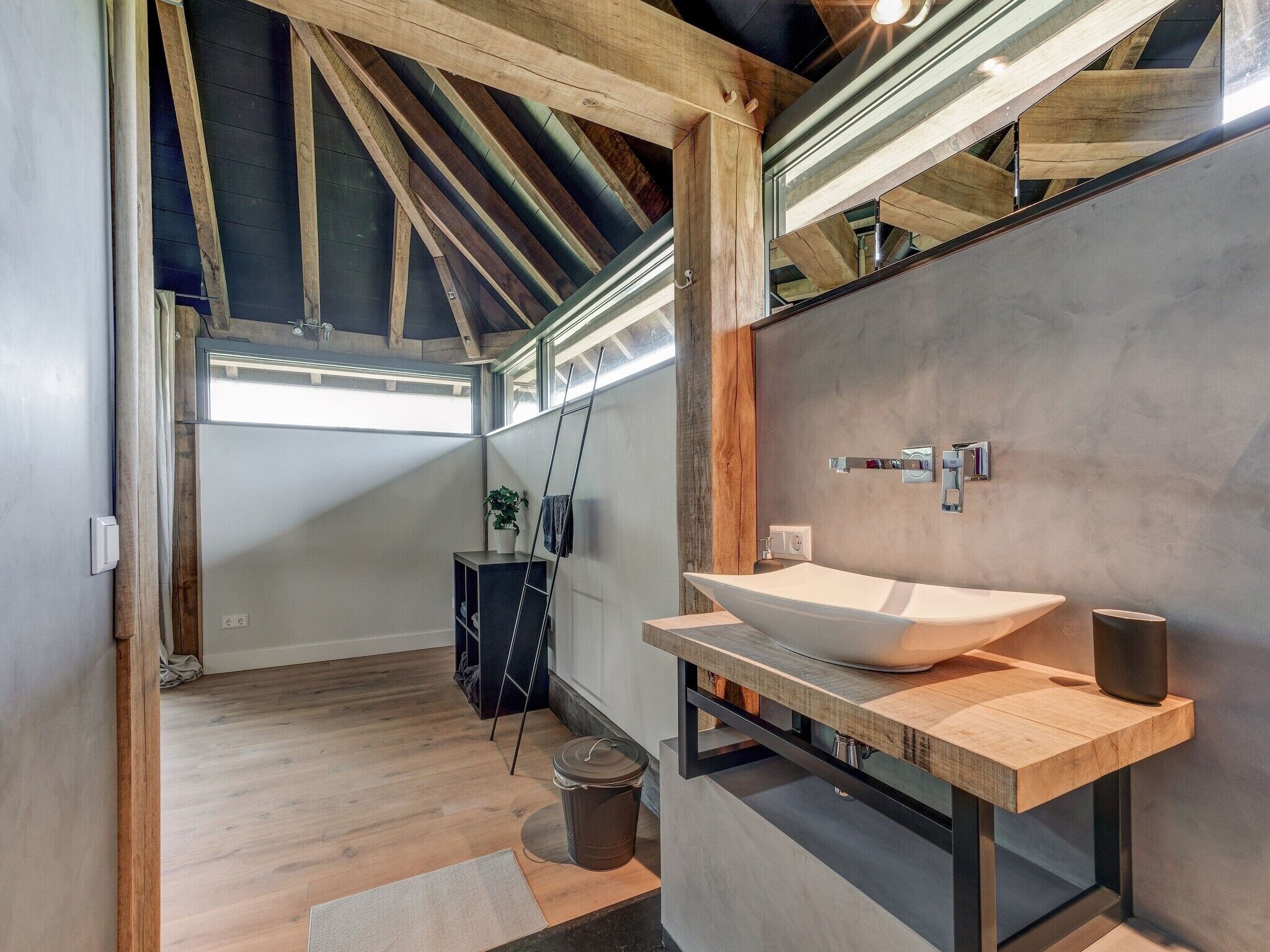 Un baño moderno con un lavamanos grande blanco, tocador de madera y techo inclinado con vigas a la vista.