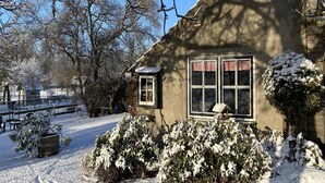 Een besneeuwde tuin met een houten huis, een bankje en een omheining.