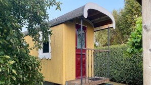 A small, yellow wooden structure with a red door and a covered porch.