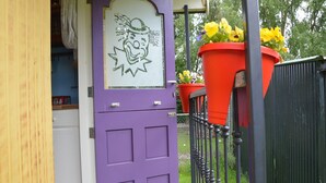 A purple door with a decorative glass panel, a metal fence, and two large flower pots with yellow and purple flowers.