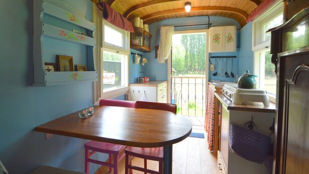 A cozy kitchen with wooden beams, a dining table with pink chairs, and a view of the garden through the window.