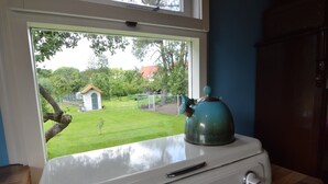 A kitchen stove with a view of a garden through a window.