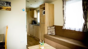 Een ruimtelijk ingerichte leefruimte met een kitchenette, een bank en een klein tafeltje met een plant.