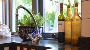 Un comptoir de cuisine agrémenté d’un robinet décoratif en métal, d’une plante en pot et de trois bouteilles de vin.