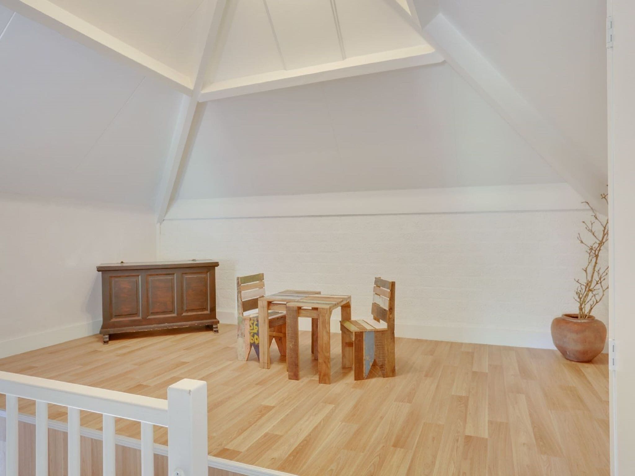 A spacious attic room with a wooden floor, a dining table with chairs, a cabinet, and a potted plant.