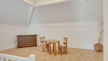 A spacious attic room with a wooden floor, a dining table with chairs, a cabinet, and a potted plant.