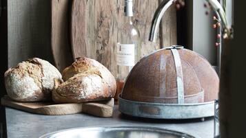 A rustic kitchen setting with a wooden cutting board, a metal sieve, and two loaves of bread.
