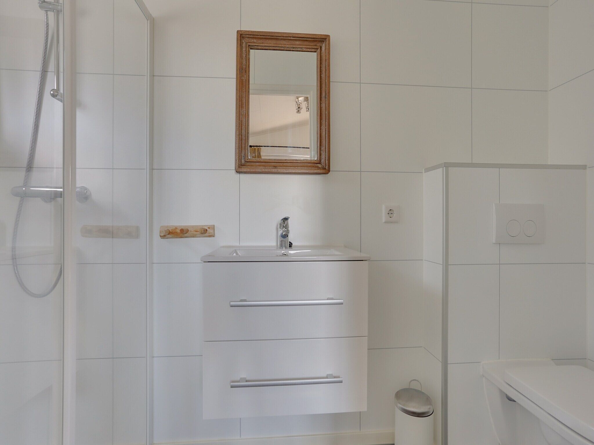 Een badkamer met een douche, een wastafel met spiegel erboven en een toilet.