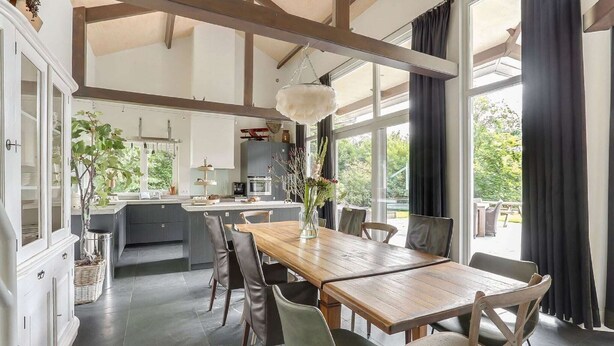 Una cocina amplia con una isla central, ventanas grandes y un comedor con mesa y sillas de madera.