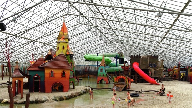 Zona de juegos interior con tobogán de agua, estructuras para escalar y un edificio con aspecto de castillo.