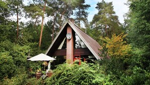 Una pequeña cabaña de techo triangular rodeada de un bosque frondoso.