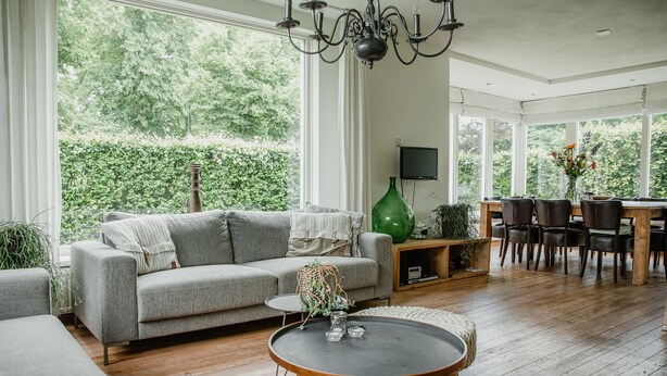 En rummelig stue med en grå sofa, et sofabord og et spiseområde med stole og et træbord.