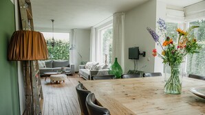 En rummelig stue med et træspisebord, to sofaer og et stort vindue med gardiner.