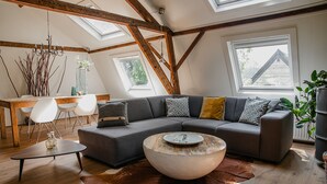 A modern loft with exposed wooden beams, a sectional sofa, a round coffee table, and a dining area with a wooden table and white chairs. - Cottage in Leenderbos with BBQ & Garden (Leende)