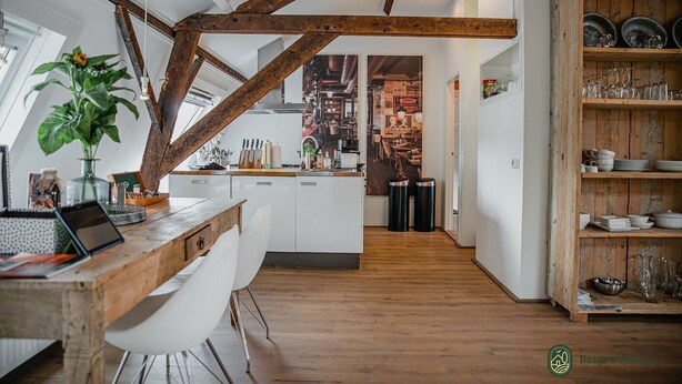 A modern kitchen with exposed wooden beams, a central island, white cabinetry, and a rustic shelving unit with dishes. - Cottage in Leenderbos with BBQ & Garden (Leende)
