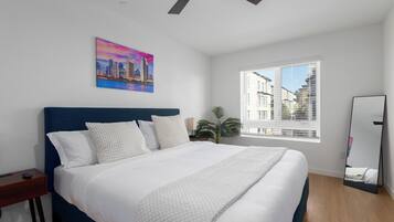 Ein Schlafzimmer mit einem großen Bett, einem Deckenventilator, einem Stadtbildgemälde, einem Fenster mit Blick auf Gebäude und einem Spiegel.