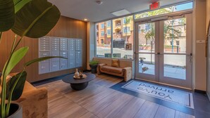 A reception area with a modern design, featuring a large plant, a seating area, and a view of the street through large glass doors.