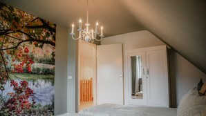A bedroom with a sloped ceiling, a chandelier, a bed, a wardrobe, and a large wall mural. - Country house next to a nature reserve (Leende)