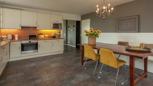 A modern kitchen with a dining area, featuring a wooden table, two yellow chairs, and a chandelier. - Country house next to a nature reserve (Leende)