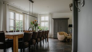 A dining area with a wooden table and chairs, large windows, and a grey cabinet. - Country house next to a nature reserve (Leende)