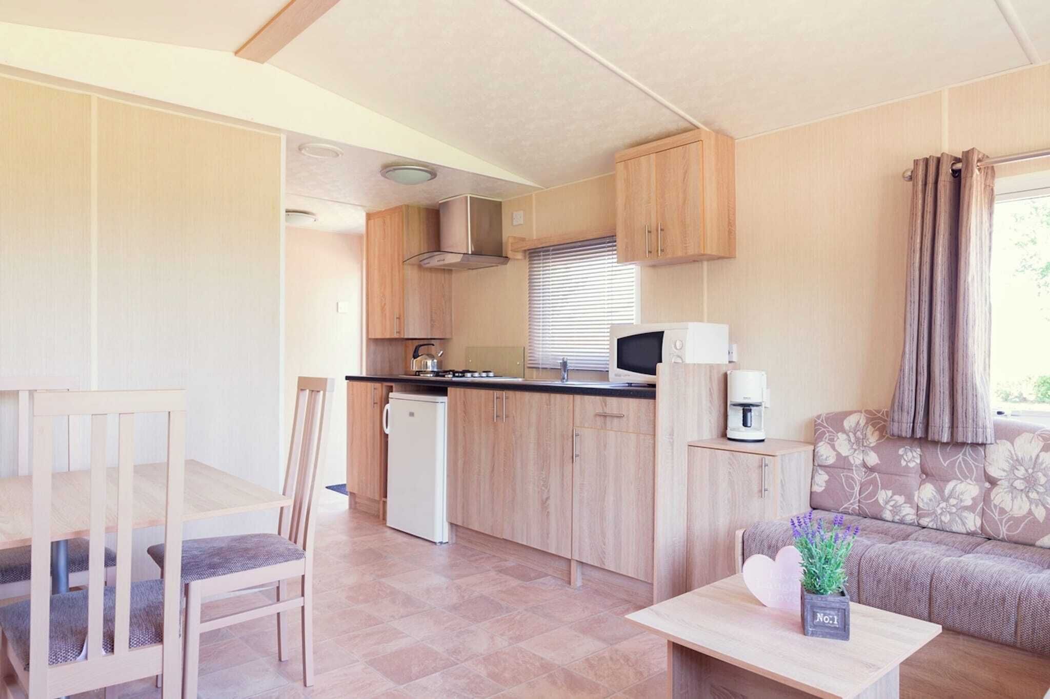 Eine kleine Küche mit Holzausstattung, einer Mikrowelle und einer Kaffeemaschine. Es gibt einen Esstisch mit Stühlen sowie eine gepolsterte Couch mit Blumenmuster.