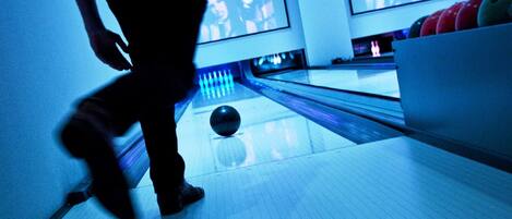 A bowling alley with a person bowling, a bowling ball, and multiple bowling lanes.