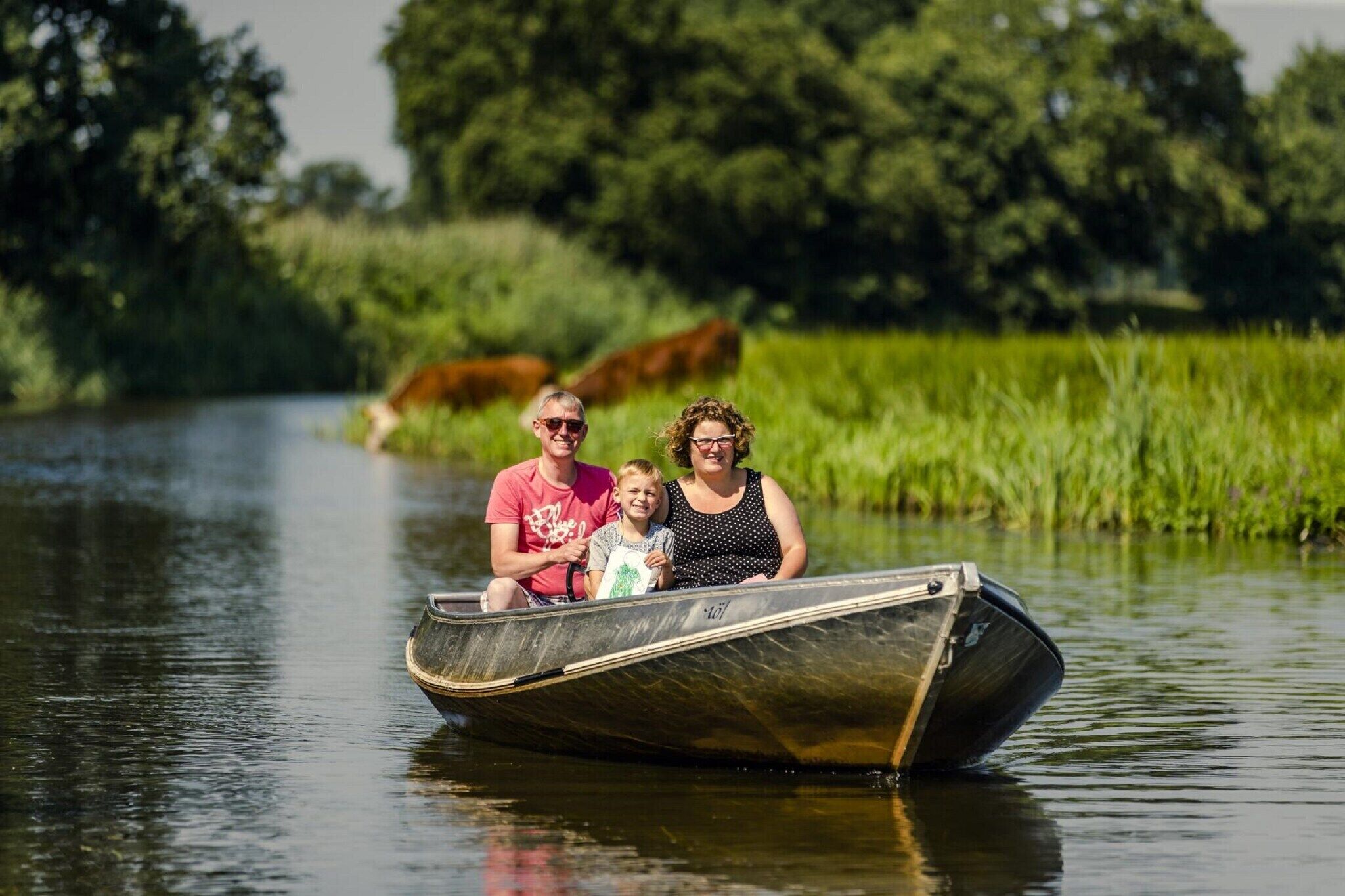 Una familia en un barco estrecho navegando por un río tranquilo, rodeada de vegetación.