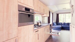 Eine moderne Küche mit Holzschränken, Edelstahlgeräten und einem eingebauten Geschirrspüler. Im angrenzenden Wohnbereich ist eine blaue Couch zu sehen.