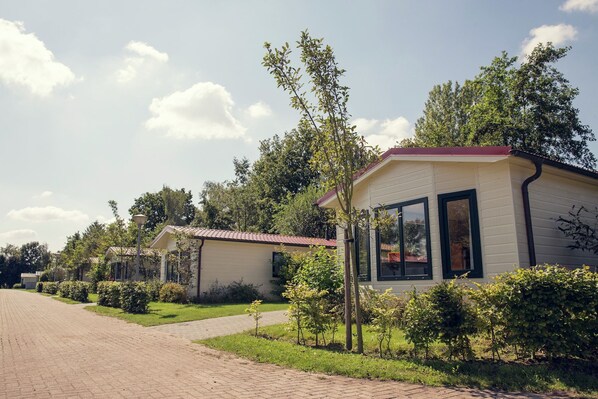A row of small, single-story buildings with a red roof, surrounded by greenery and a clear sky. - Riverside Chalet Retreat (Zuna)