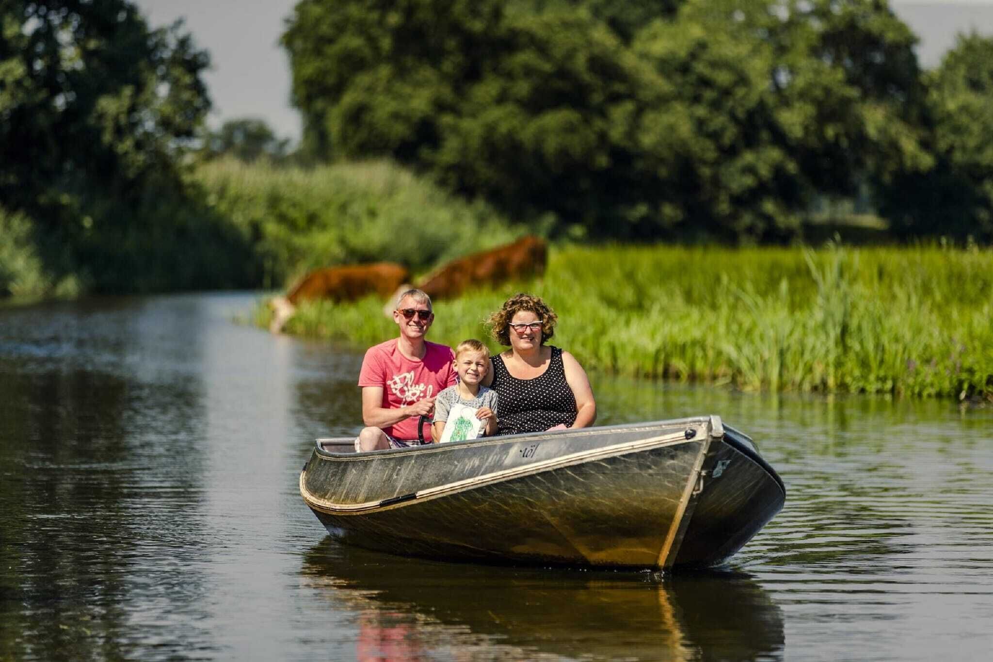 Une famille se trouve à bord d’un étroit bateau sur une rivière paisible, entourée de verdure.