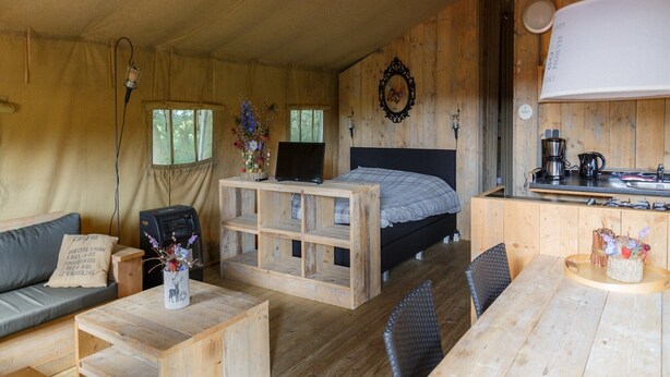 A cozy cabin interior with a bed, a desk, a dining table, and a kitchenette.