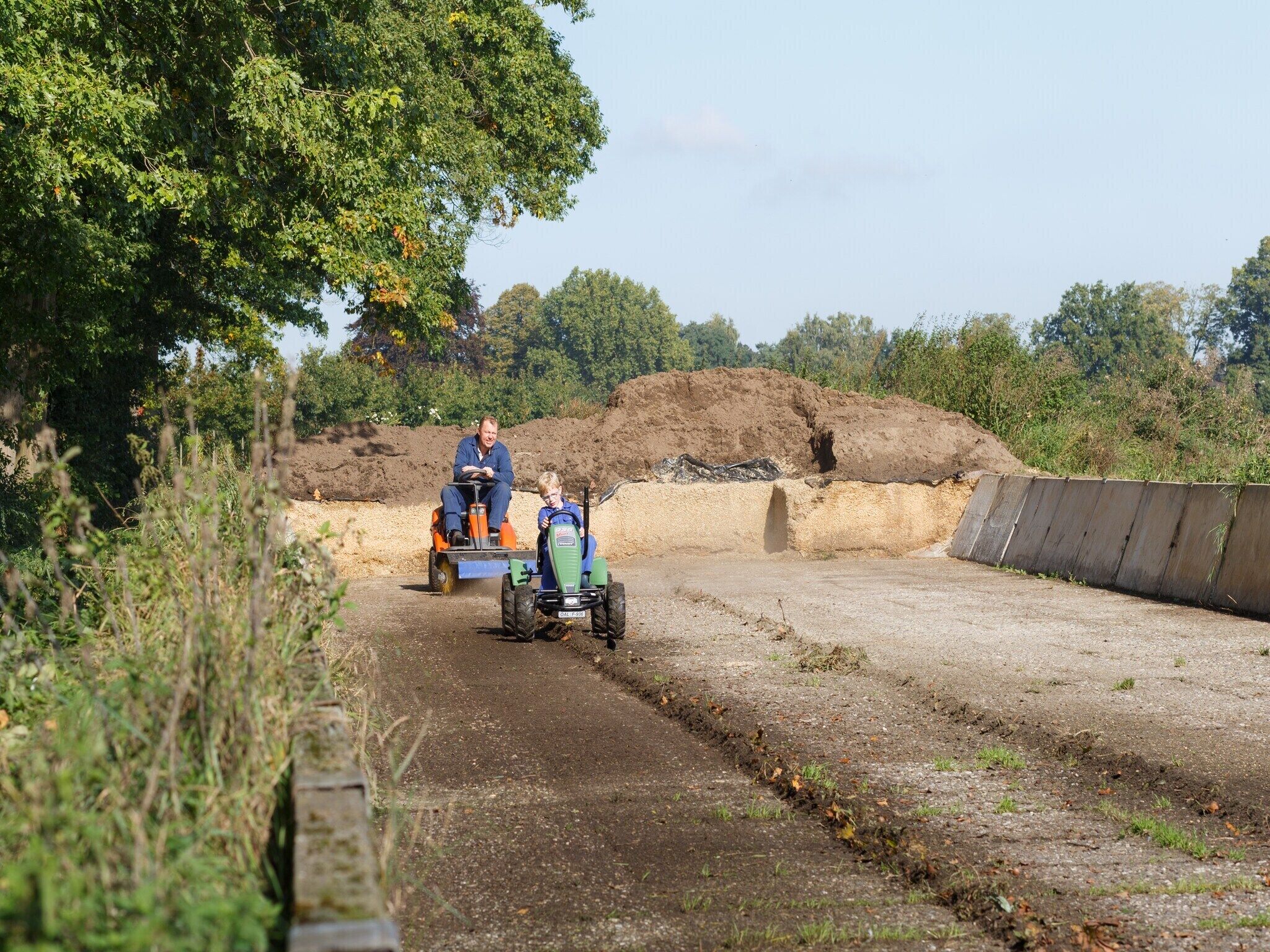 A dirt road with two tractors, one with a person and one with a child.