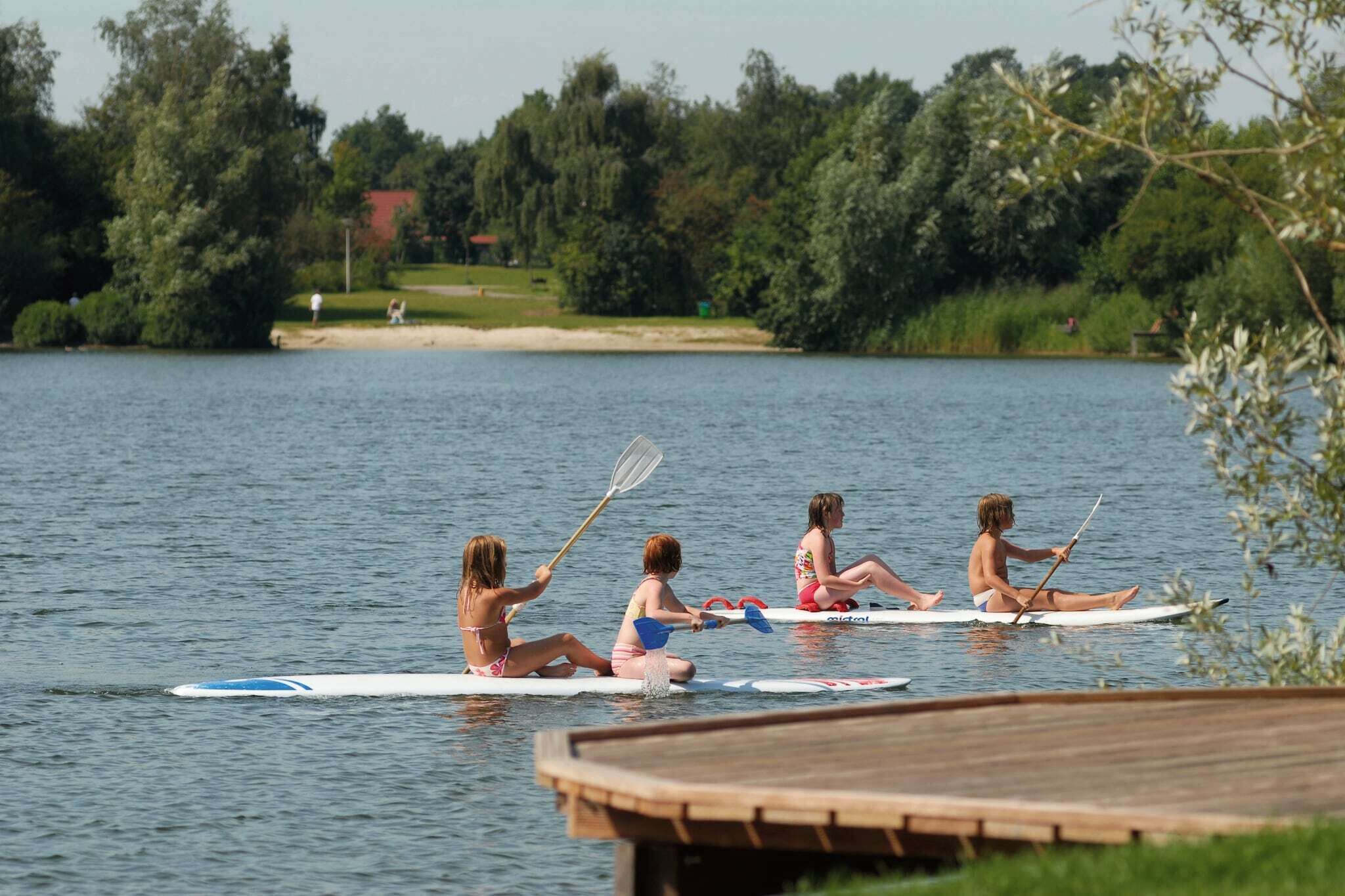 A group of people on paddleboards in a calm lake with a dock in the foreground.