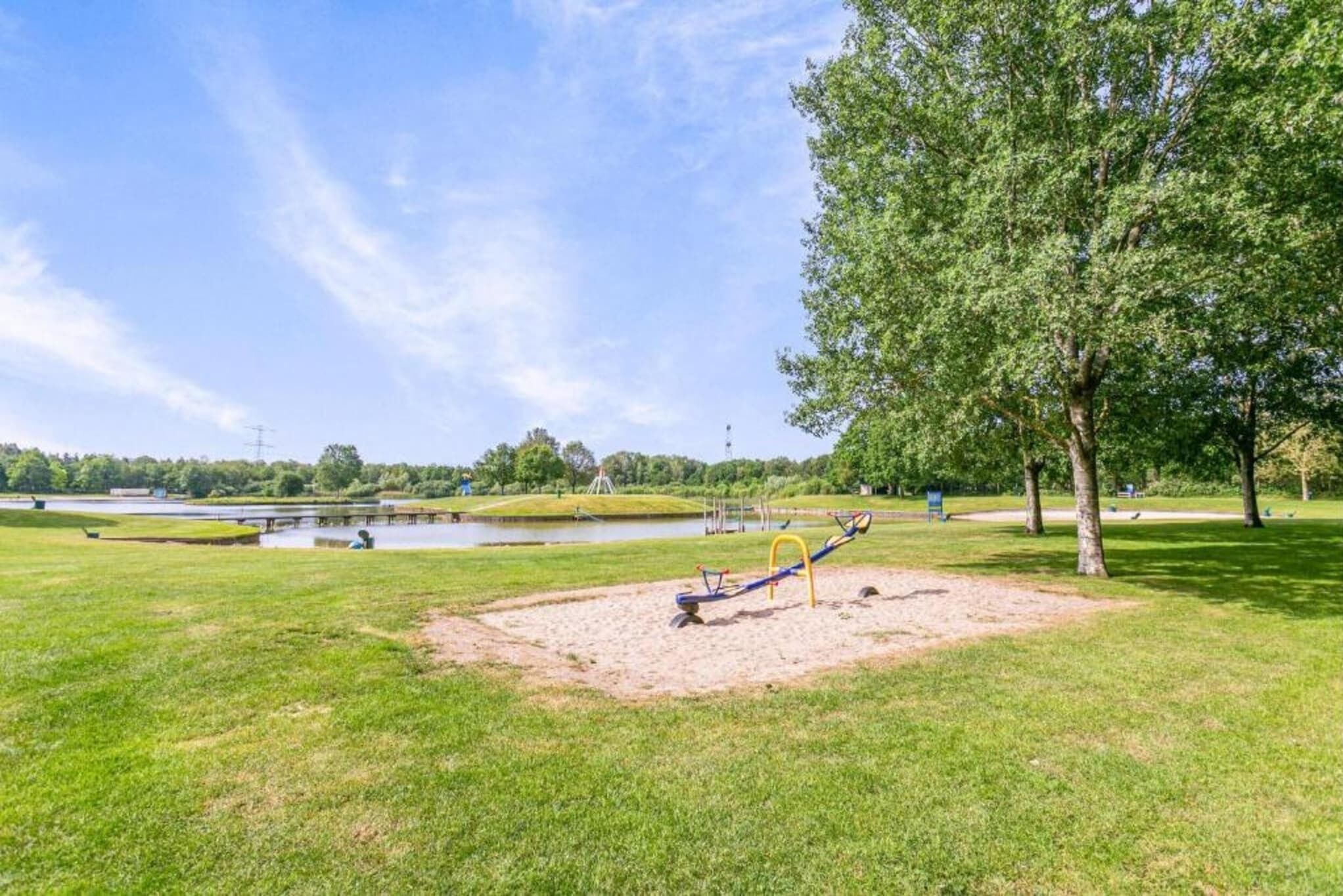A park with a sandy play area, a pond, and trees.