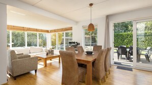 Un vaste salon doté d’une table à manger en bois, de canapés beige et d’une grande porte-fenêtre coulissante donnant sur une terrasse extérieure.