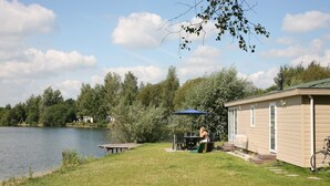 A lakeside cabin with a dining area and a covered patio. - Holiday home in park in Twente (Hoge Hexel)