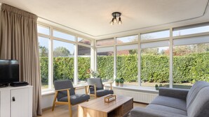 A modern living room with a large window, a flat-screen TV, a wooden coffee table, and a grey sofa. - Holiday home in park in Twente (Hoge Hexel)