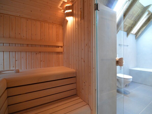 A sauna room with wooden walls and a glass door leading to a bathroom with a toilet and a bathtub. - Stylish Farmhouse with Private Garden and Sauna (Nieuwleusen)