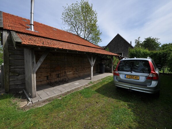 A rustic wooden building with a tiled roof, a parked car, and a tree in the background. - Stylish Farmhouse with Private Garden and Sauna (Nieuwleusen)