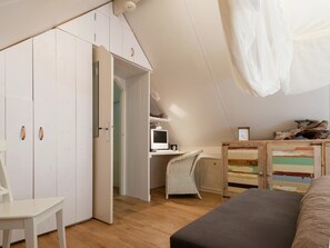 Un dormitorio con techo inclinado, un escritorio con computadora, una silla, una cama y un armario.